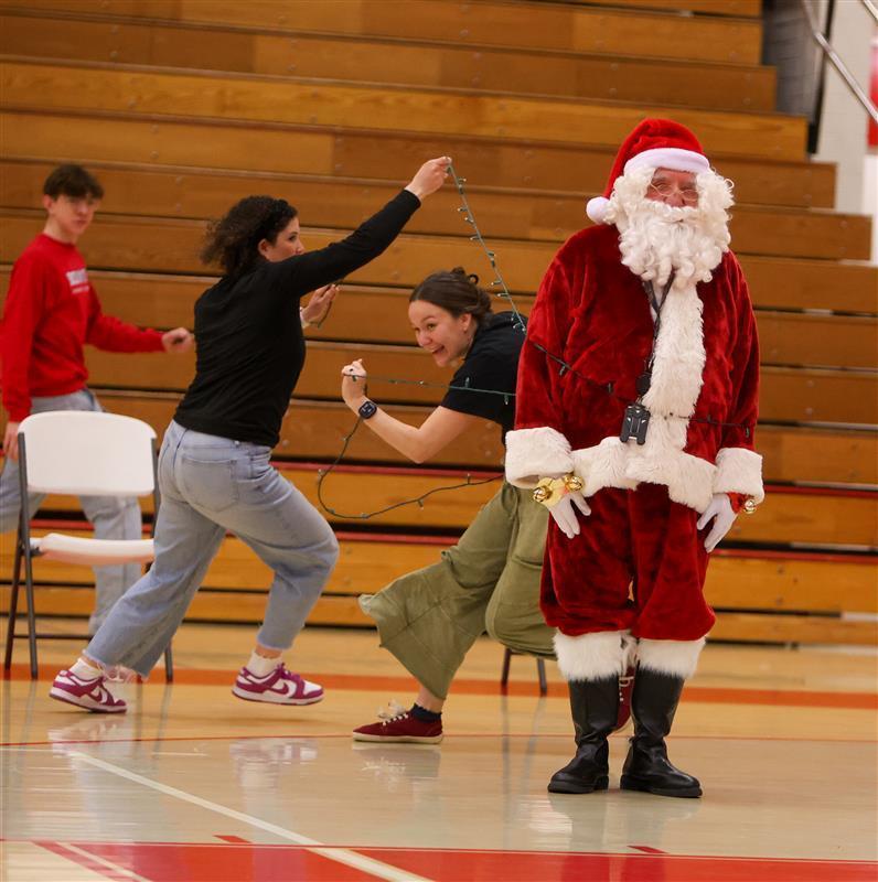 two adults wrapping lights around santa
