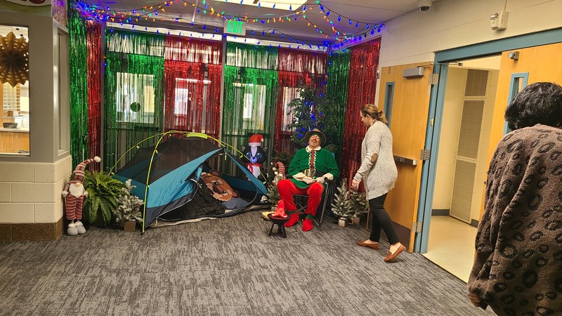 Pinky the Elf in front of a decorated hallway throwing marshmellows at students.