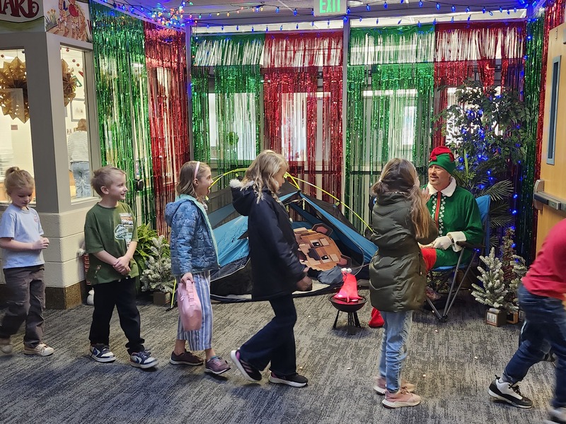 Pinky the Elf in front of a decorated hallway throwing marshmellows at students.