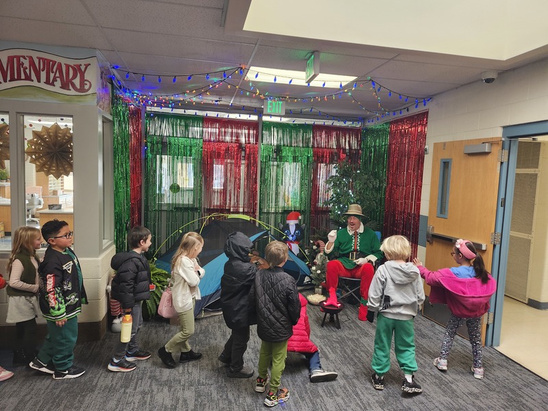 Pinky the Elf in front of a decorated hallway throwing marshmellows at students.
