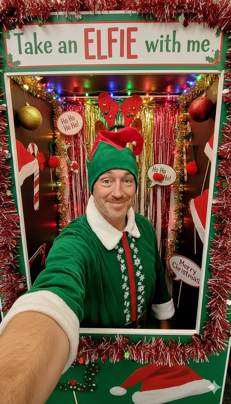 Pinky the elf taking a selfie with a sign that says Take an Elfie with me.