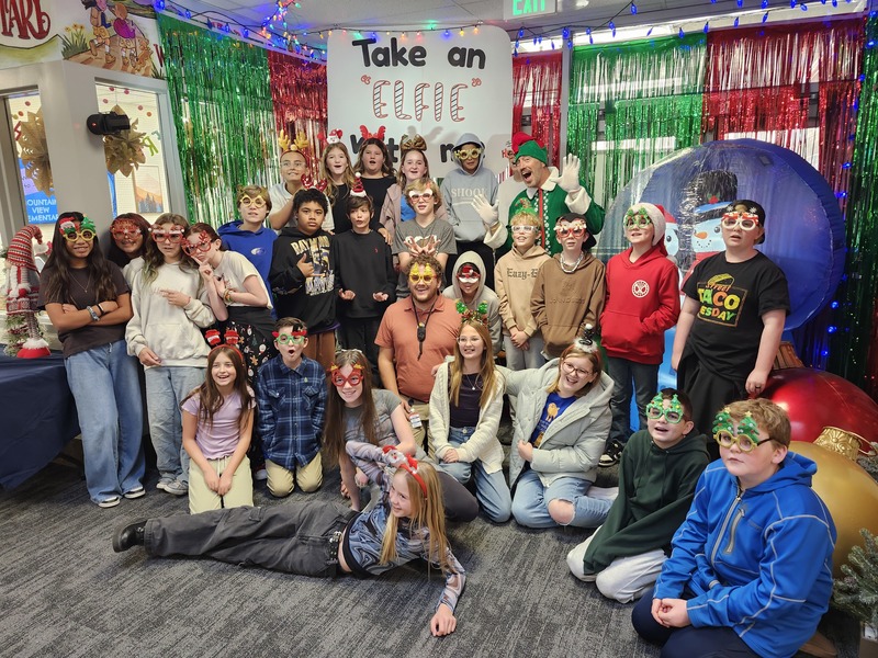 Children posing with Pinkie the Elf in front of decorations and a sign that says Take an "Elfie" with me.