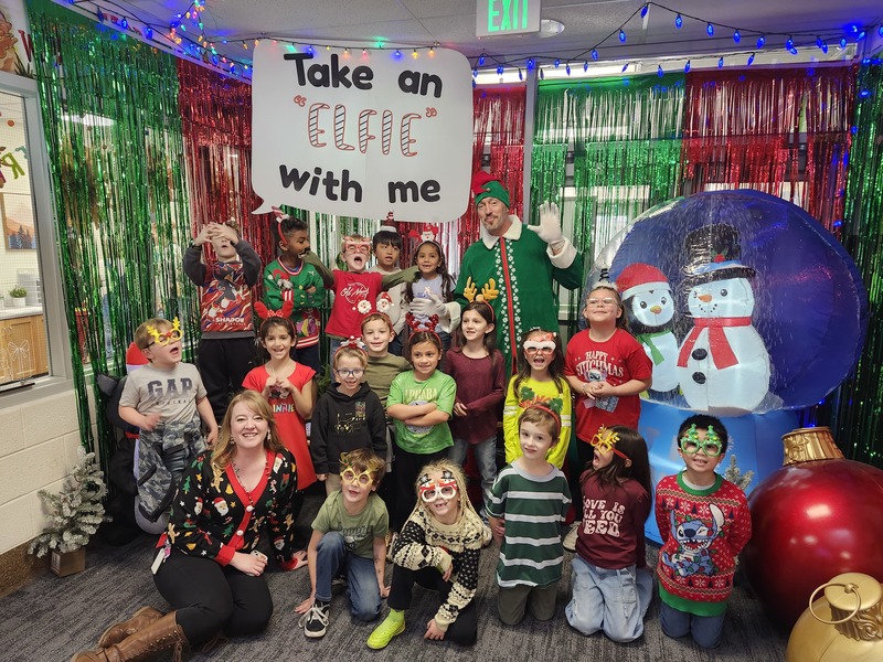 Children posing with Pinkie the Elf in front of decorations and a sign that says Take an "Elfie" with me.