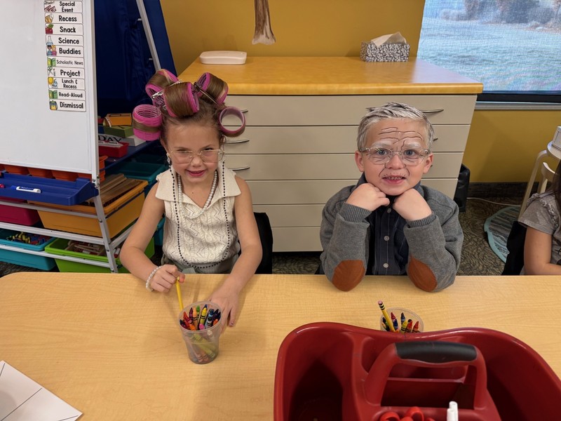 Students dressed as 100 year olds at a desk in a classroom