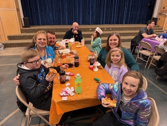 Stuednets with their families eating lunch with an orange tablecloth