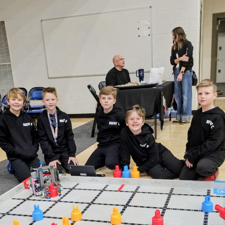Five Bountiful elementary students from THE 4BIDDEN5 VEX IQ robotics team pose beside their robot and field during the state robotics competition, wearing matching black team hoodies.