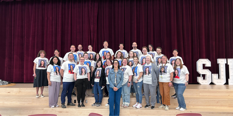 Principal Tami Oliver surrounded by several staff members and teacher wearing t-shirts showcasing several school pictures of Mrs. Oliver throughout the years.
