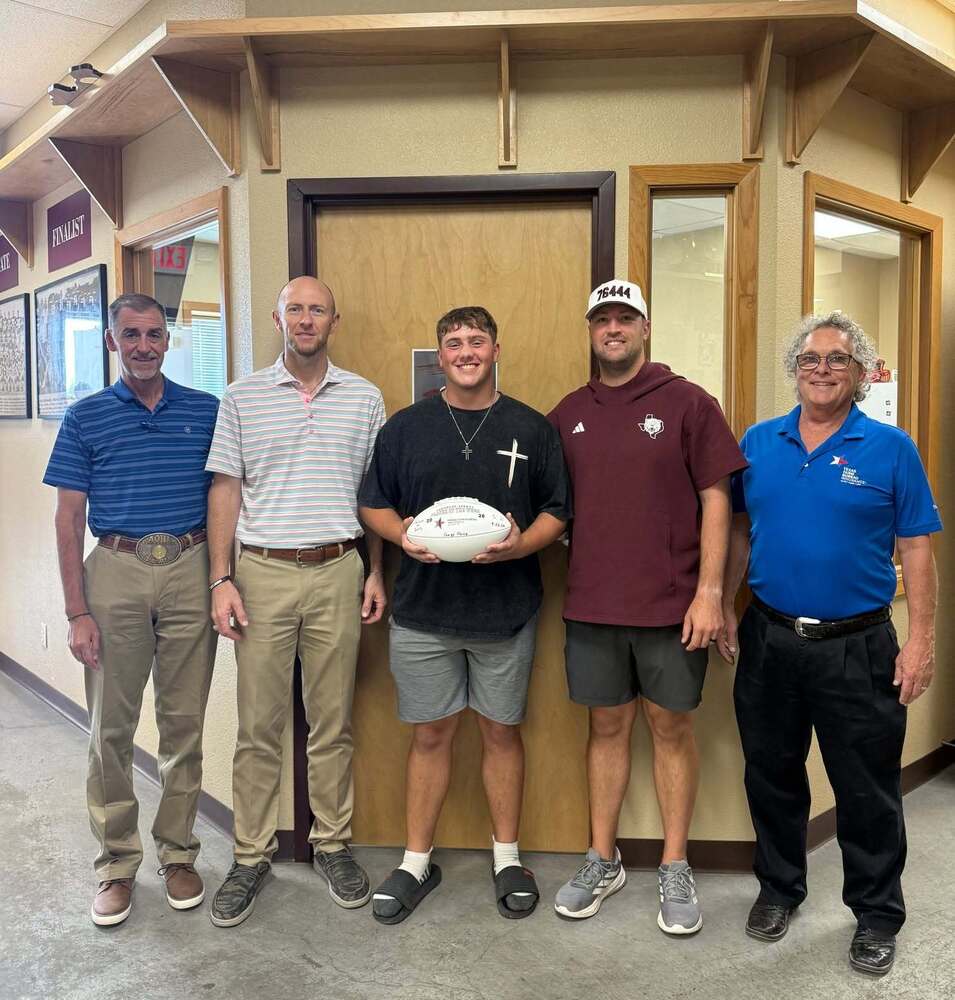 player of the week standing in the middle of four men in front of field house office