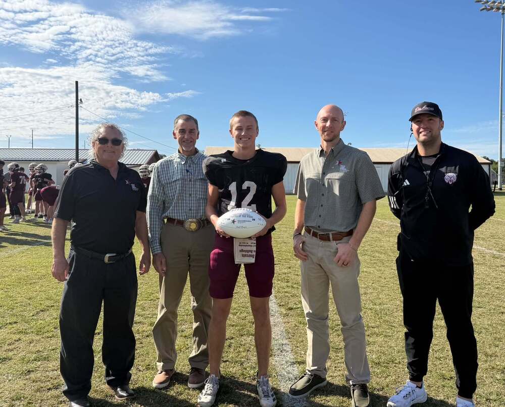 three men from local insurance company standing with football player and coach on football field