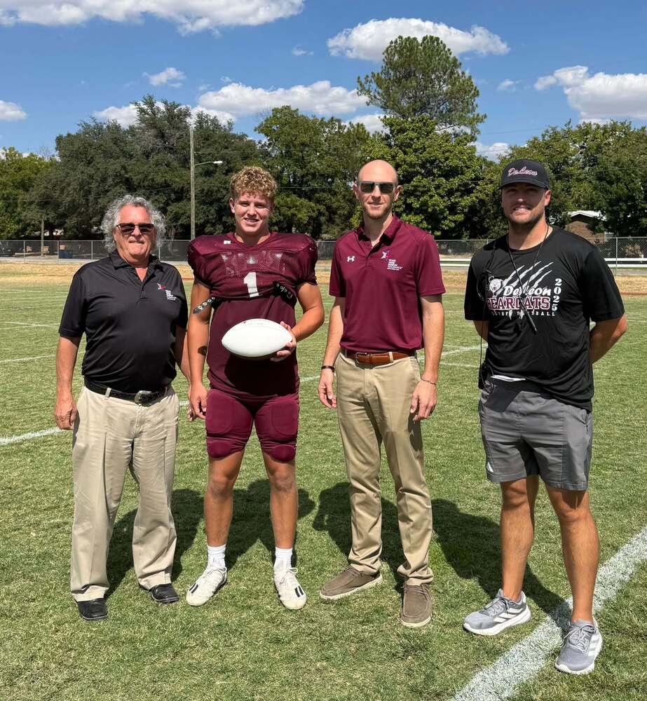 two insurance agency reps standing with player of the week and head coach on practice field