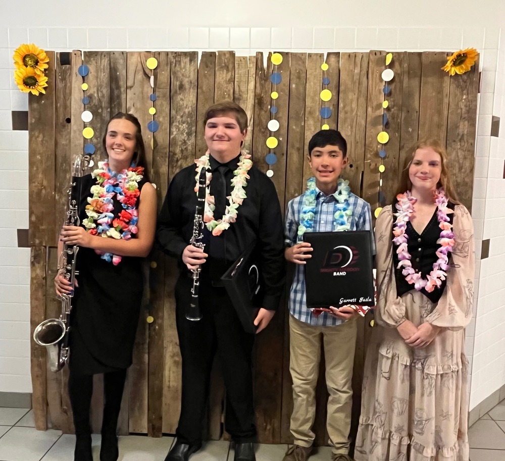four eighth grade students with their instruments in front of wood pallet backdrop