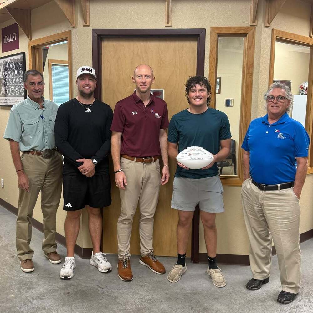 three insurance agents, football coach and varsity player of the week holding football, all standing in front of coach's office