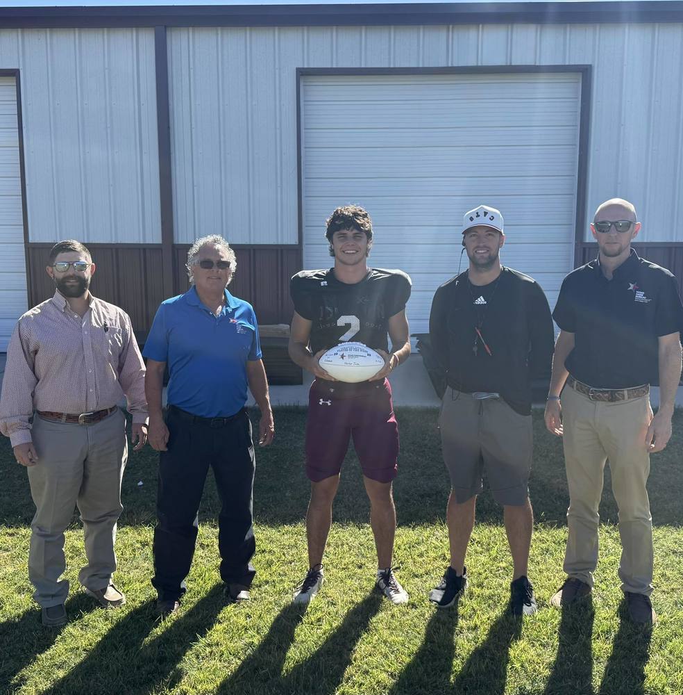 football player standing with four men in front of field house