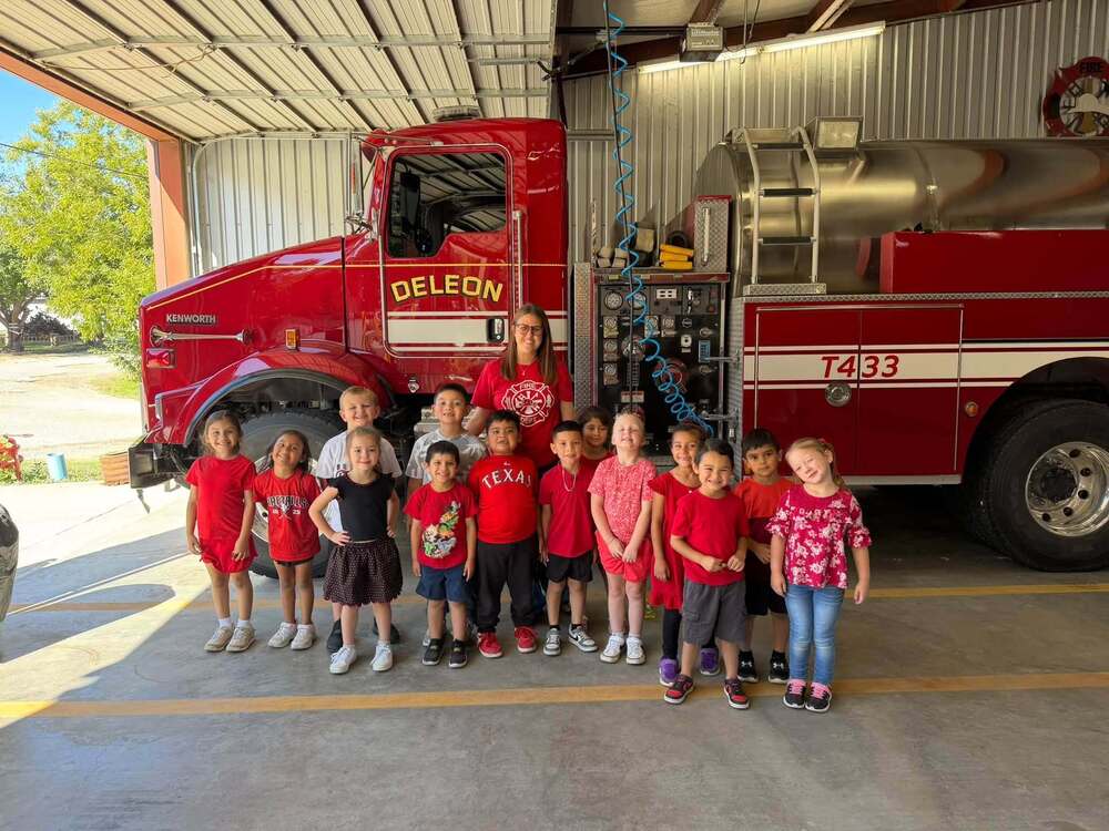 group of kindergarteners and teacher standing in front of fire truck in fire house