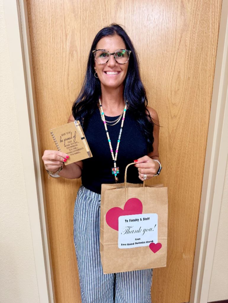 teacher holding brown gift bag and small brown notebook