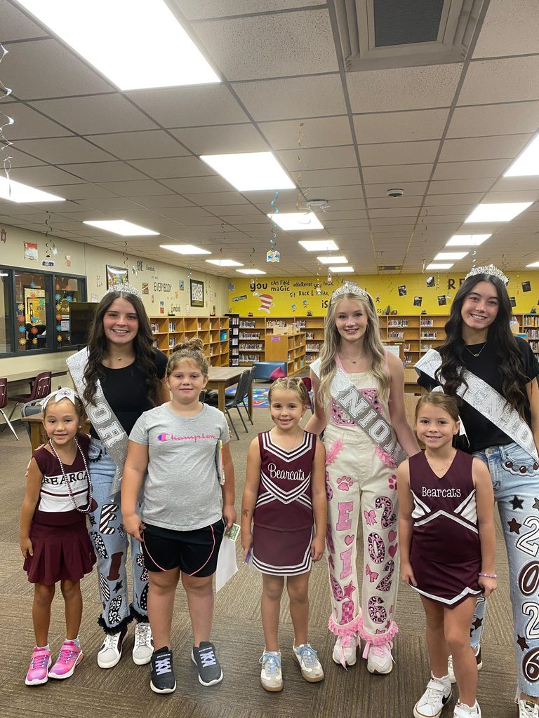 three cheerleaders posing with four girls in library