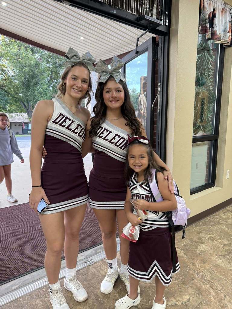two cheerleaders posing with an elementary student dressed in cheer suit