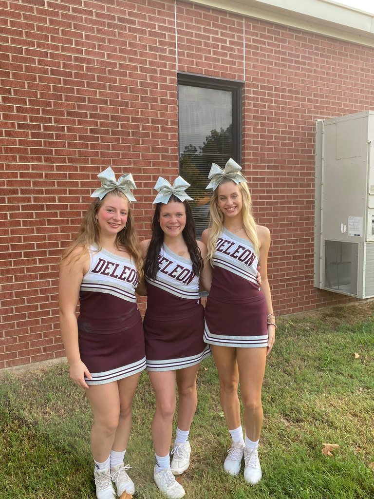 three cheerleaders posing next to elementary building
