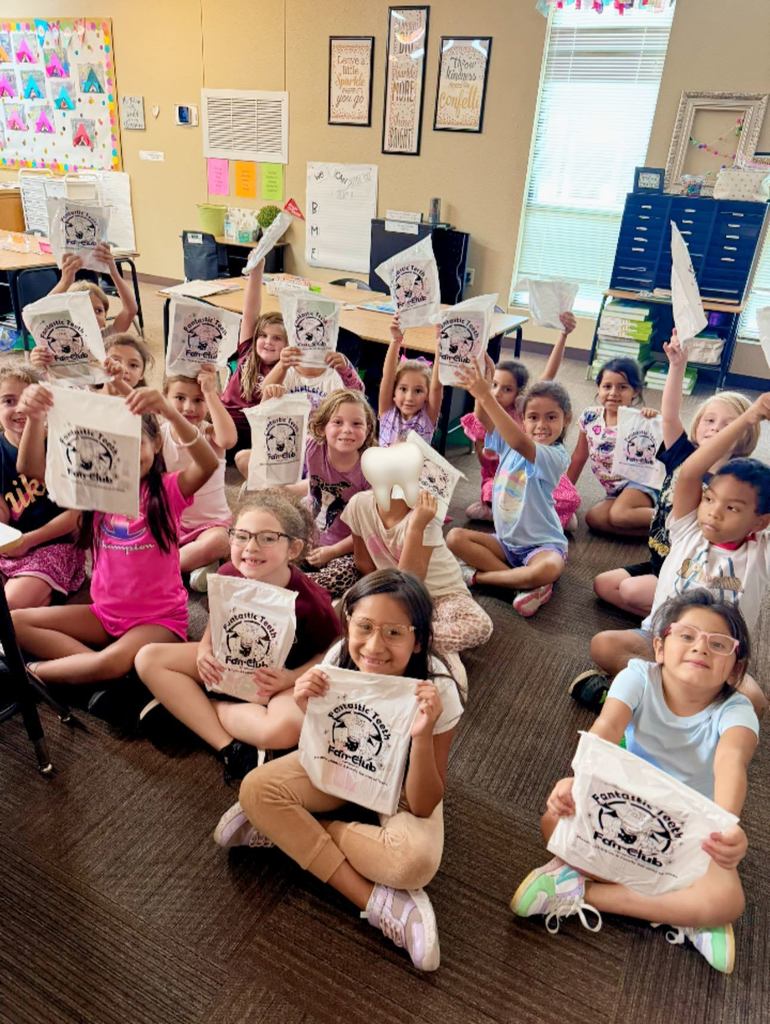 class of students sitting on floor holding up gift bags