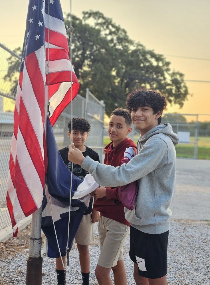three students getting ready to raise flags up pole