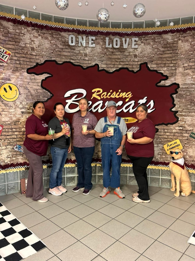 five custodians holding drinks in the foyer of high school