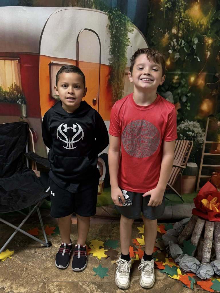 two campers of the week standing in front of campfire backdrop