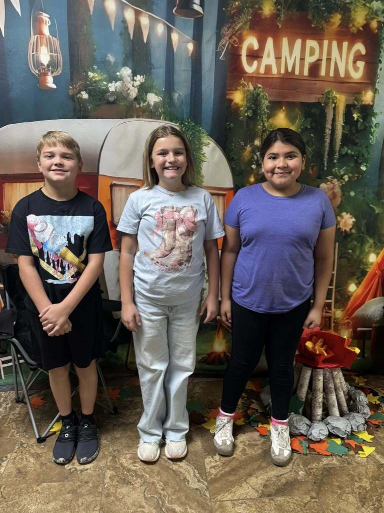 three campers of the week standing in front of campfire backdrop