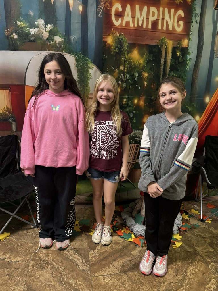 three campers of the week standing in front of campfire backdrop