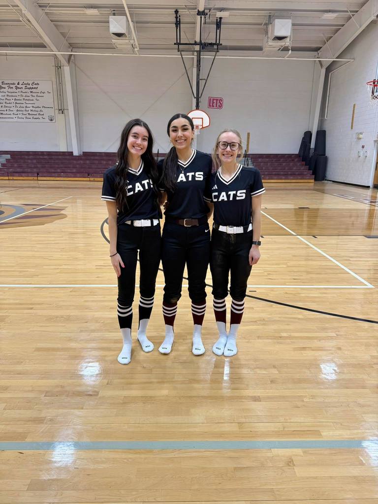 three senior softball players modeling new uniforms in gym