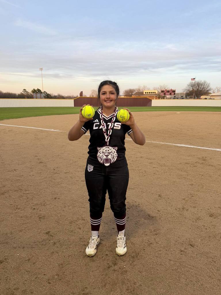 softball player holding a softball in each hand while standing on field