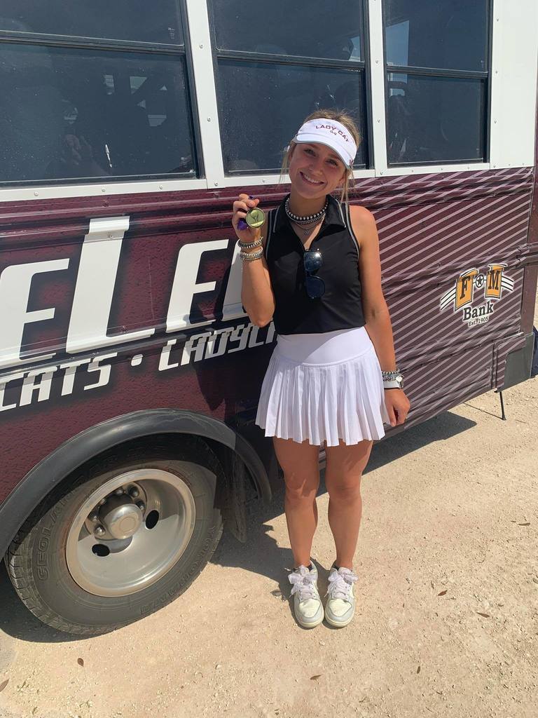 female golfer holding gold medal standing next to activity bus