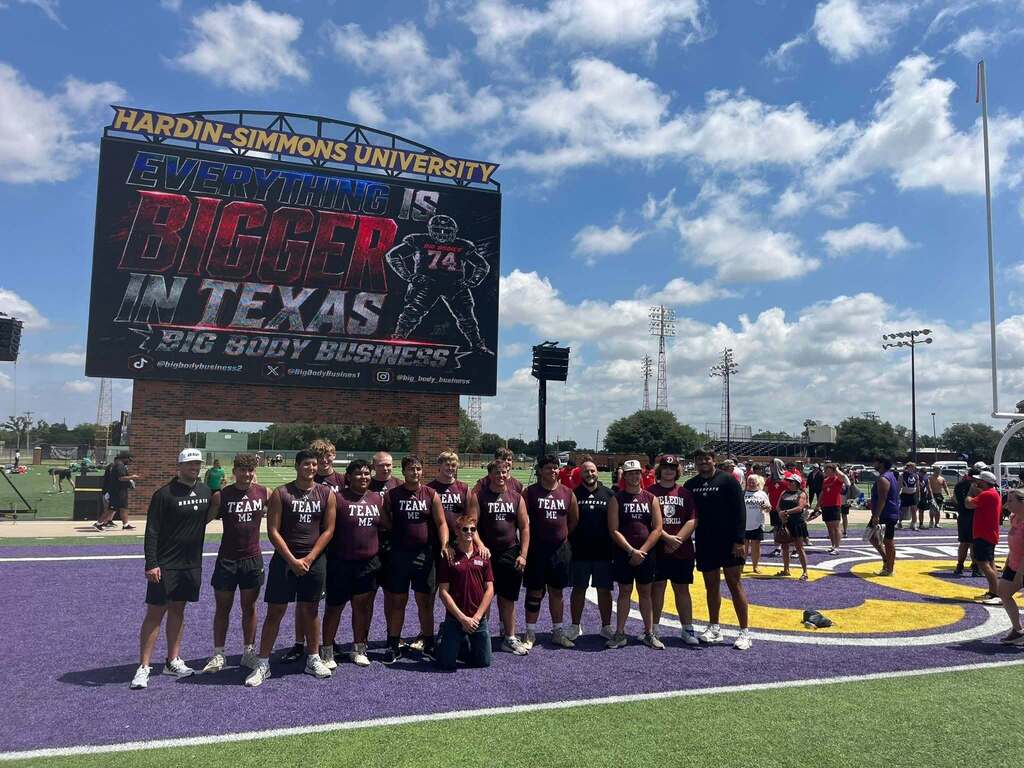 group of football linemen and coaches standing on football field