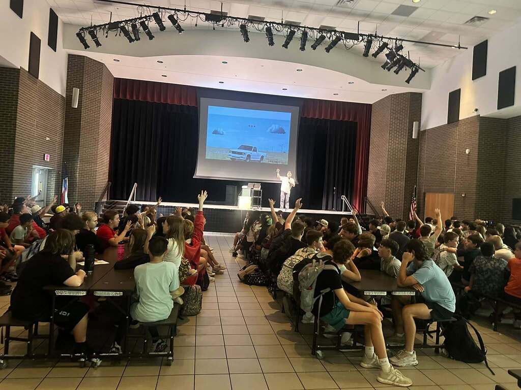 cafeteria full of middle school students participating with guest speaker standing on stage