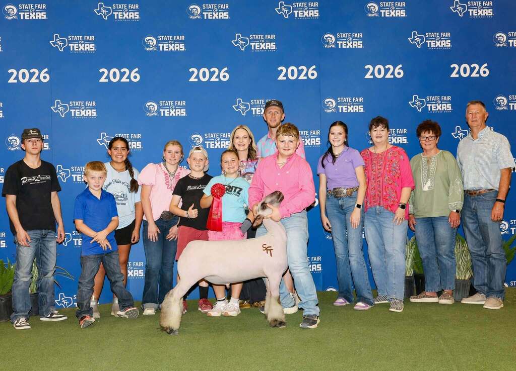 FFA student standing with show animal, family members, friends and lady holding yellow ribbon