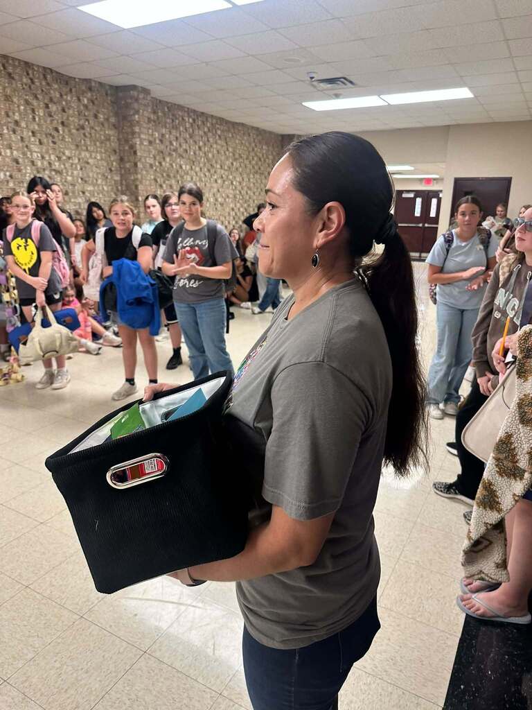 custodian holding black box full of goodies and standing in hallway surrounded by students