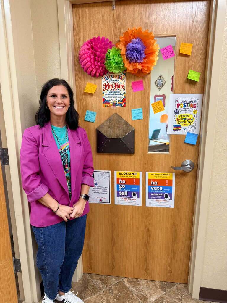 staff member standing in front of door decorated with flyers, post-its, and colorful paper flowers