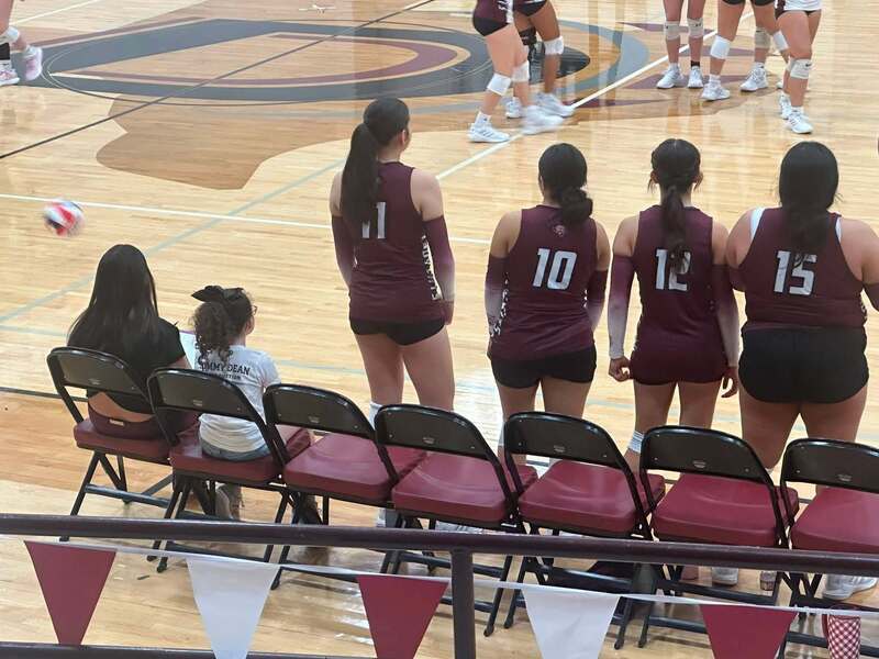 volleyball players standing along bench and two girls sitting at end of bench