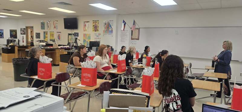 students sitting in desks with red gift bags sitting on top with speaker looking in their direction