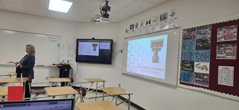 guest speaker looking towards students with whiteboard and display in background