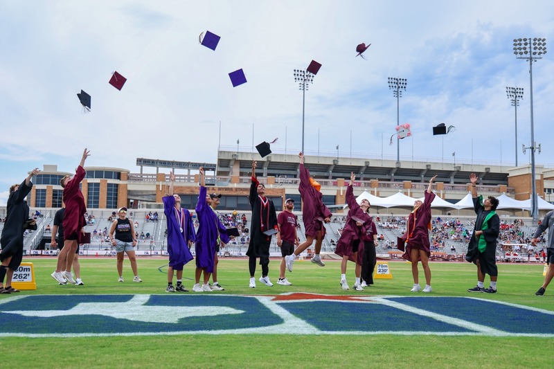 graduates throwing their caps in the air while standing on field