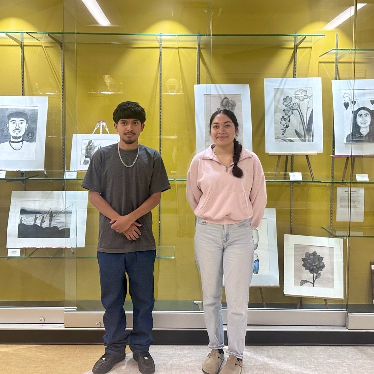 Jesus and Anahi standing in front of their art work in trophy case