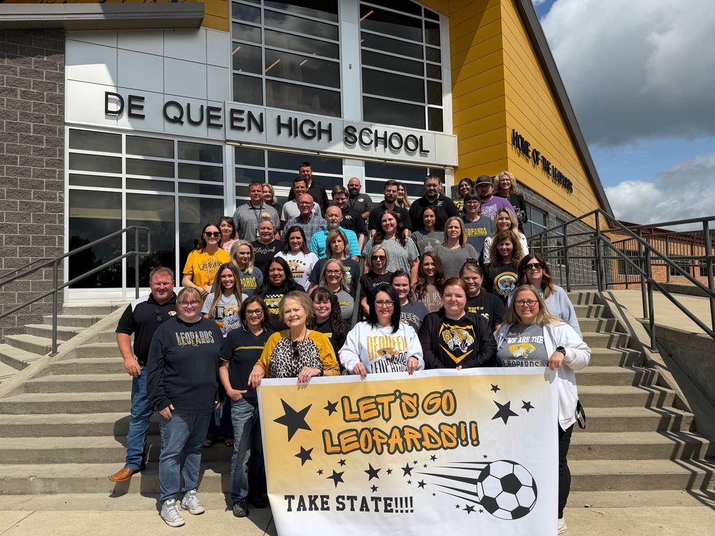 DHS faculty standing in front of high school holding soccer banner