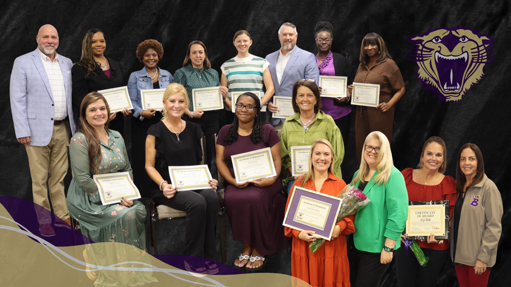 Group photo of Decatur County Schools honorees standing and seated with certificates, including members of the Aspiring Administrative Cohort and award recipients, posed against a black backdrop with the Bearcat logo.