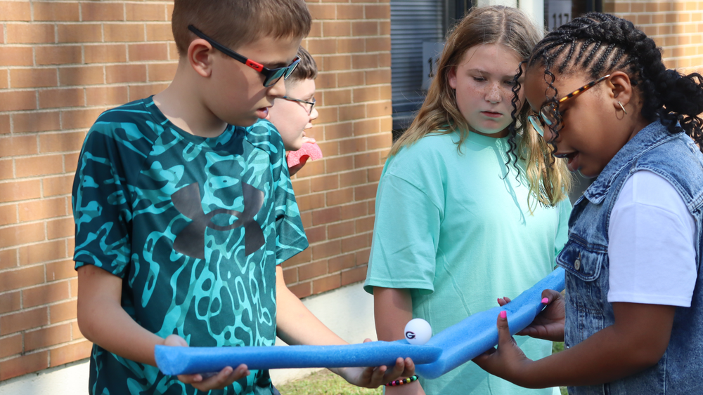 Two students work together to guide a ball through colorful foam tubes during a hands-on STEM activity.
