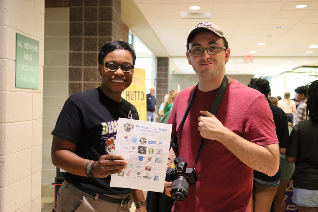 Two individuals pose with a Bearcat Blitz Bingo card at the community event.