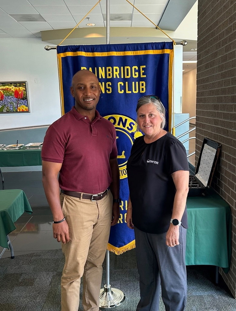 Head Baseball Coach Ryan Riles poses with a member of the Bainbridge Lions Club in front of a Lions Club banner during a recent meeting.