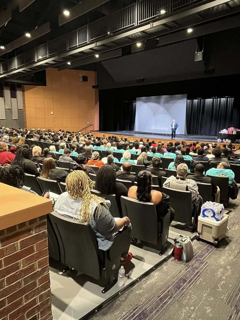 A large audience of school nutrition staff seated in an auditorium listening to a speaker on stage at Bainbridge High School.