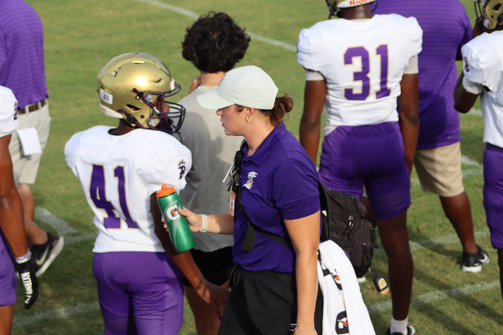A Bainbridge High School athletic trainer in a white cap hands a water bottle to a football player wearing jersey number 41 on the sideline during a game or practice.