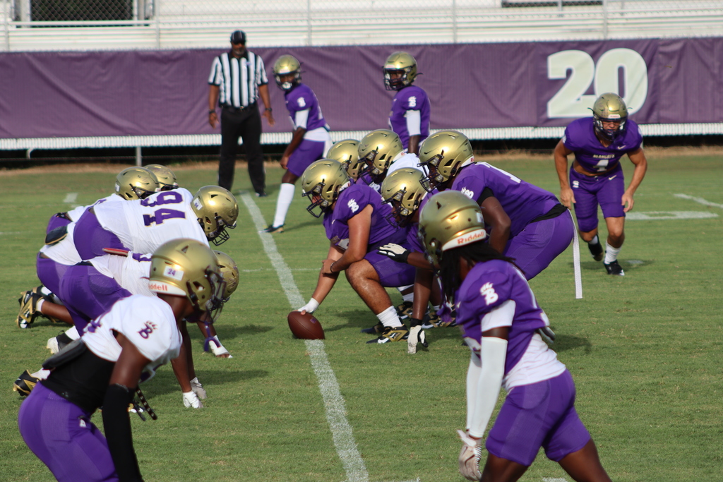 Bainbridge High School football players line up at the line of scrimmage during a practice scrimmage, with a referee observing in the background.