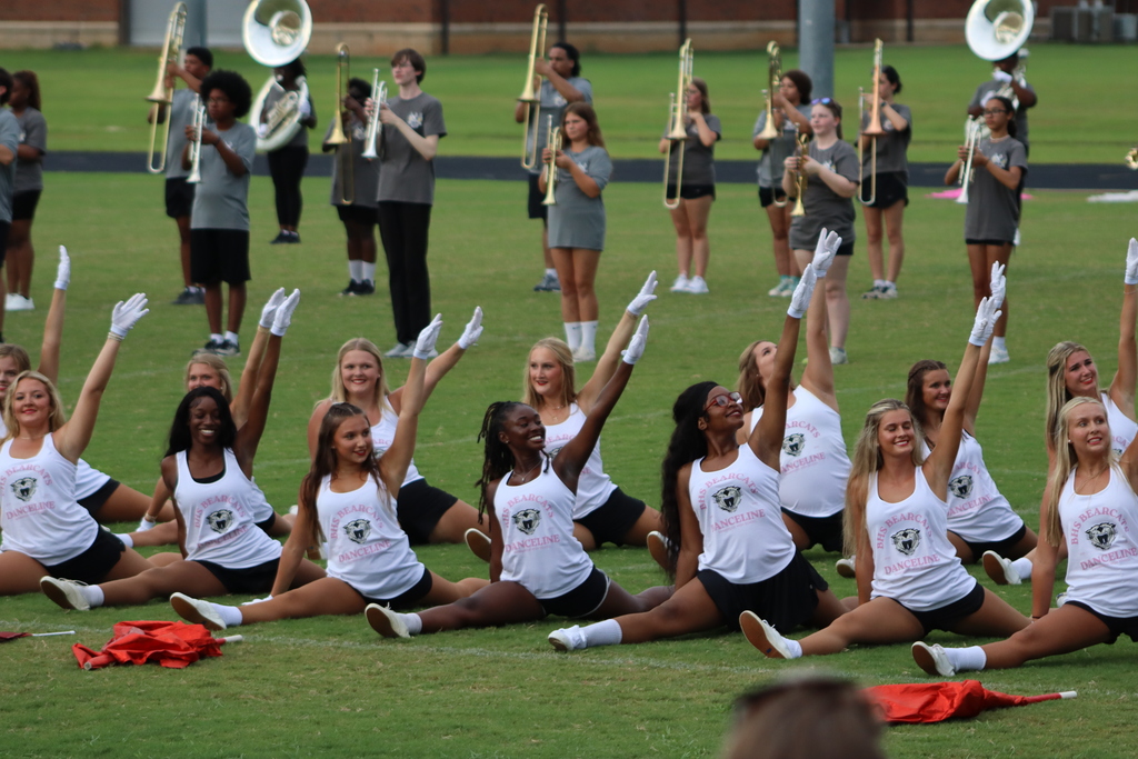 Danceline members finish their performance with a synchronized pose in splits and arms raised while the marching band continues playing behind them